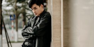 Self assured young man in a trendy black leather jacket standing with arms folded on a city street