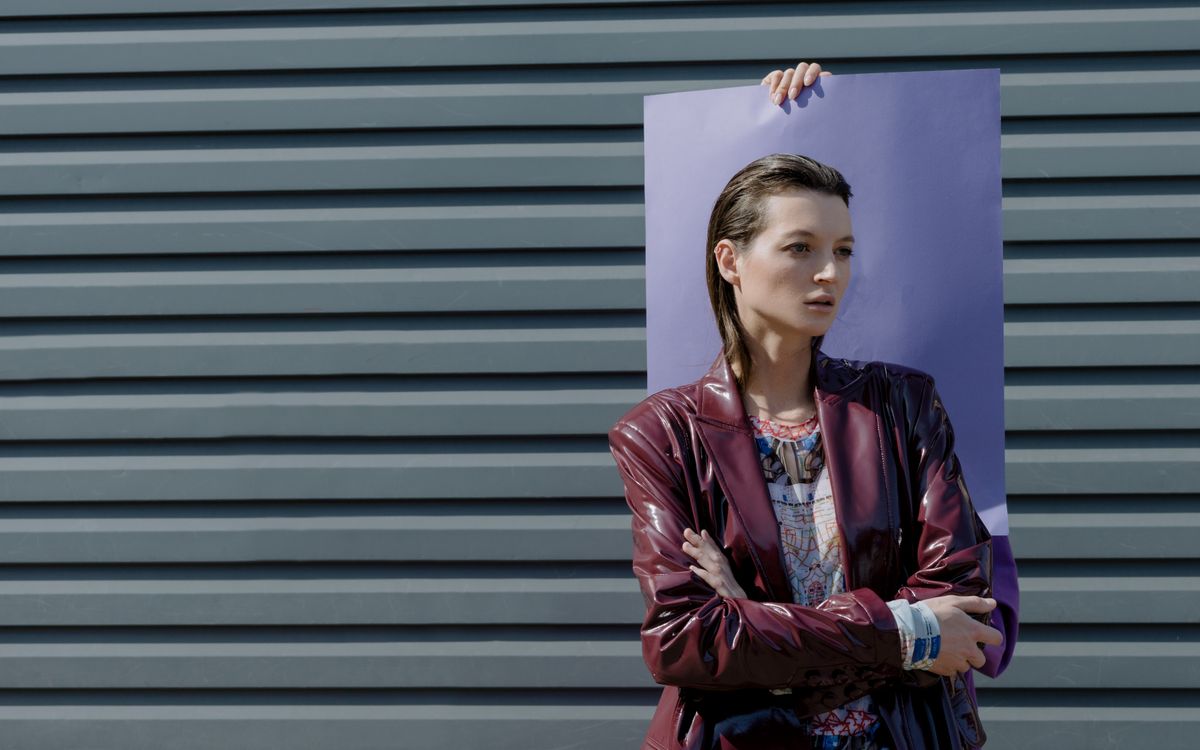Fashionable woman in a burgundy leather jacket posing against a modern background in daylight