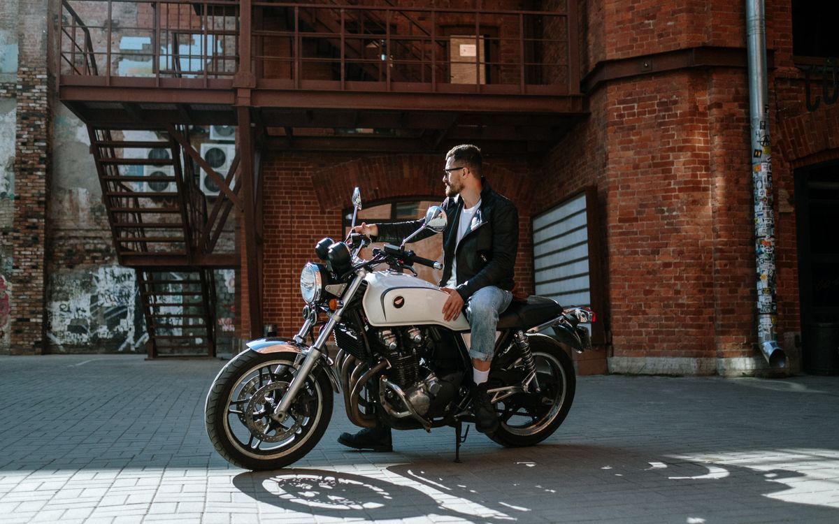 Man in a leather biker jacket sitting on a motorcycle by an urban brick building