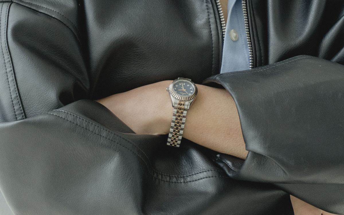 Close-up of a watch worn over a leather jacket sleeve, showing the grain and stitching