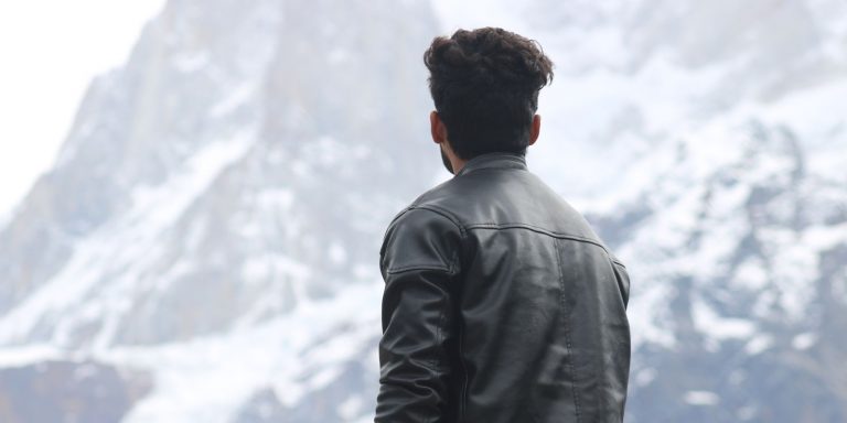 A man in a leather jacket gazing at snow-covered mountains under a clear winter sky