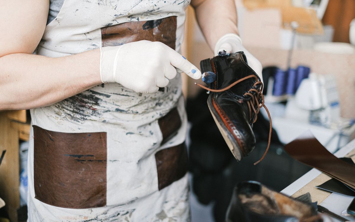 A craftsman in gloves works conditioner into leather in a workshop, restoring its finish