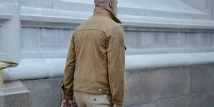 Man in a stylish brown leather jacket walking past a classic city building