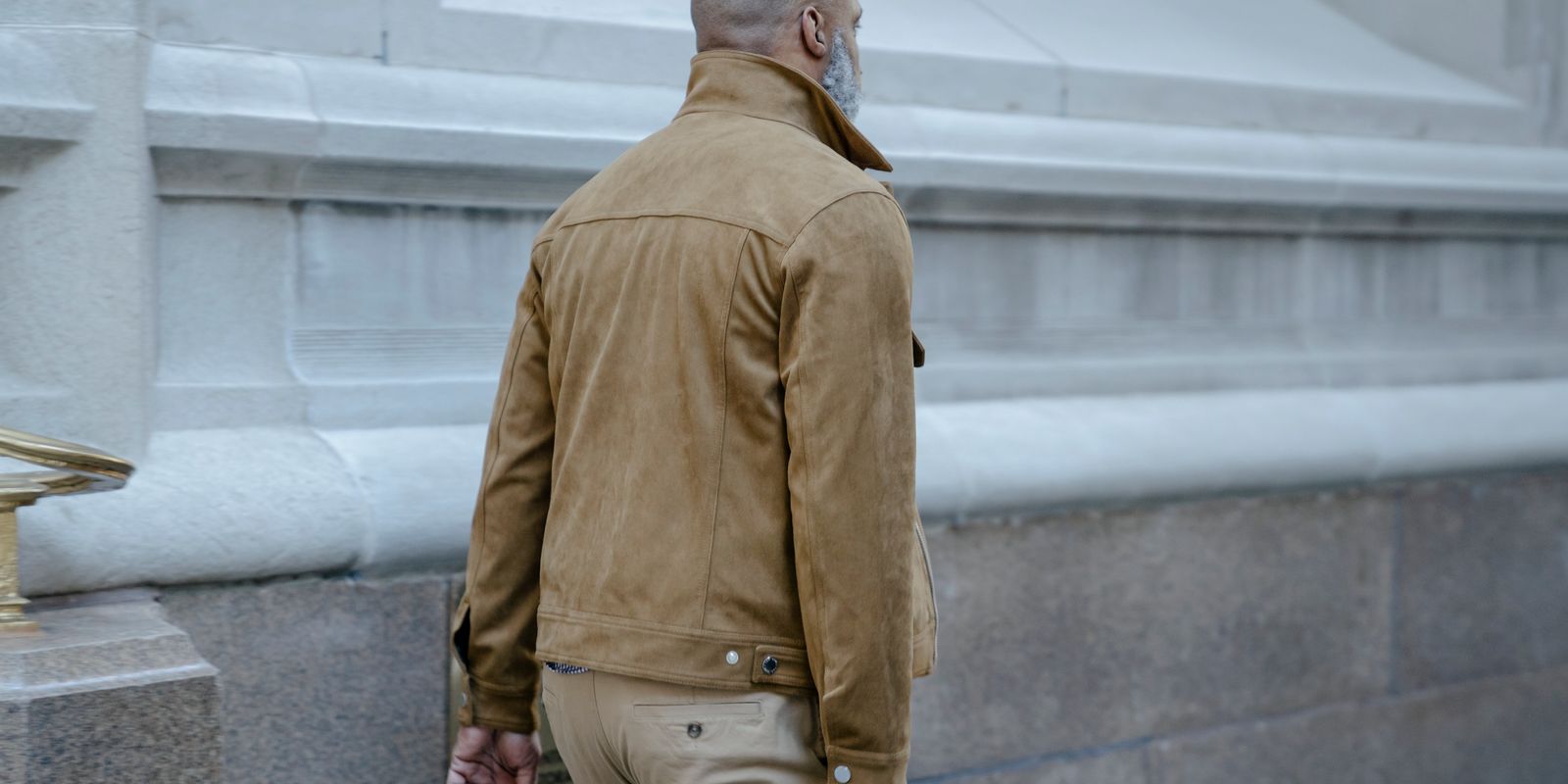 Man in a stylish brown leather jacket walking past a classic city building