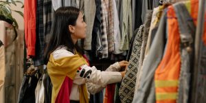 A young woman browsing a rack of clothing in a vintage store full of colorful outfits