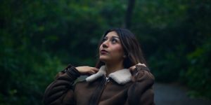 Woman in a warm brown leather jacket on a lush forest path