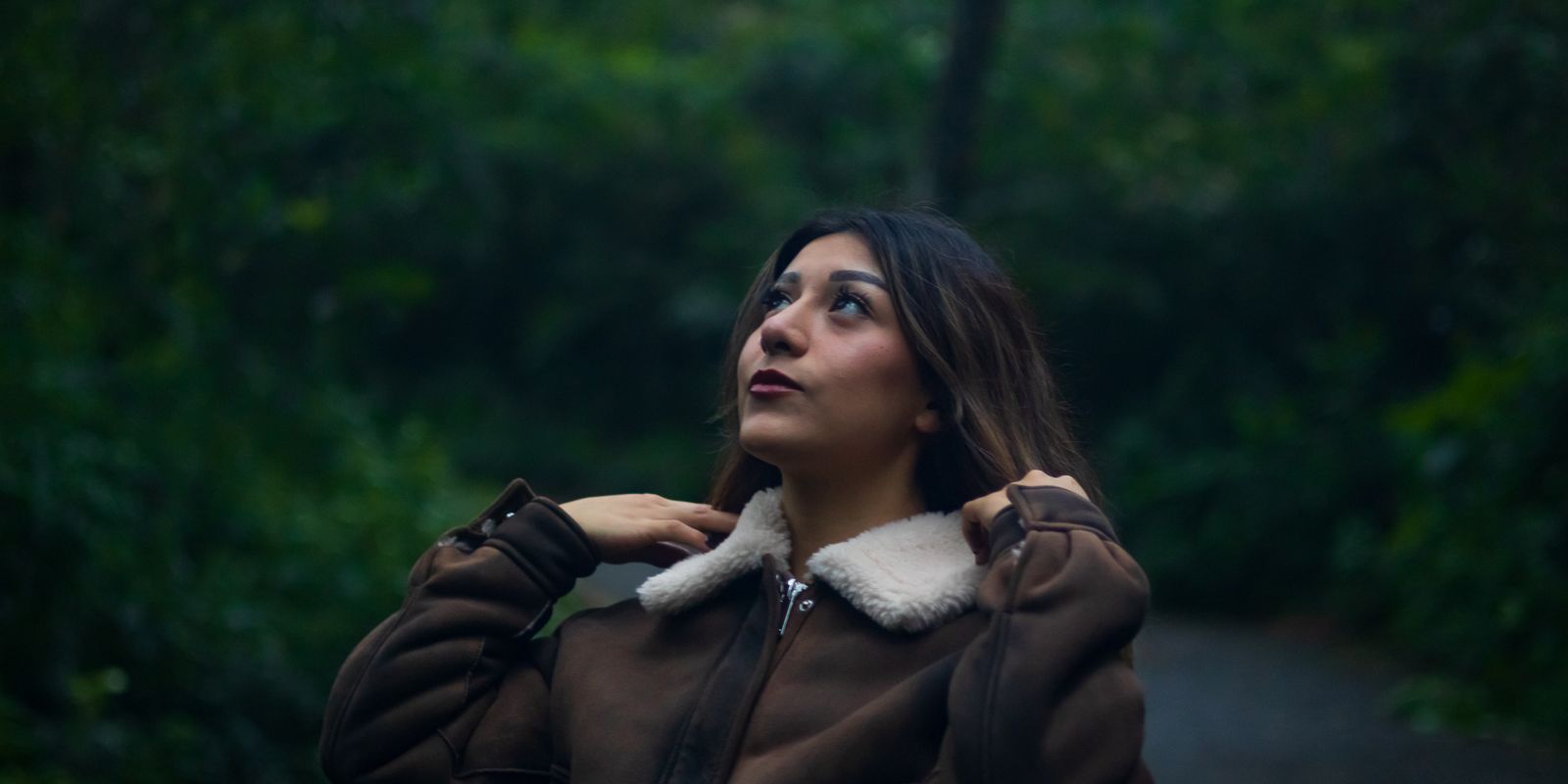 Woman in a warm brown leather jacket on a lush forest path