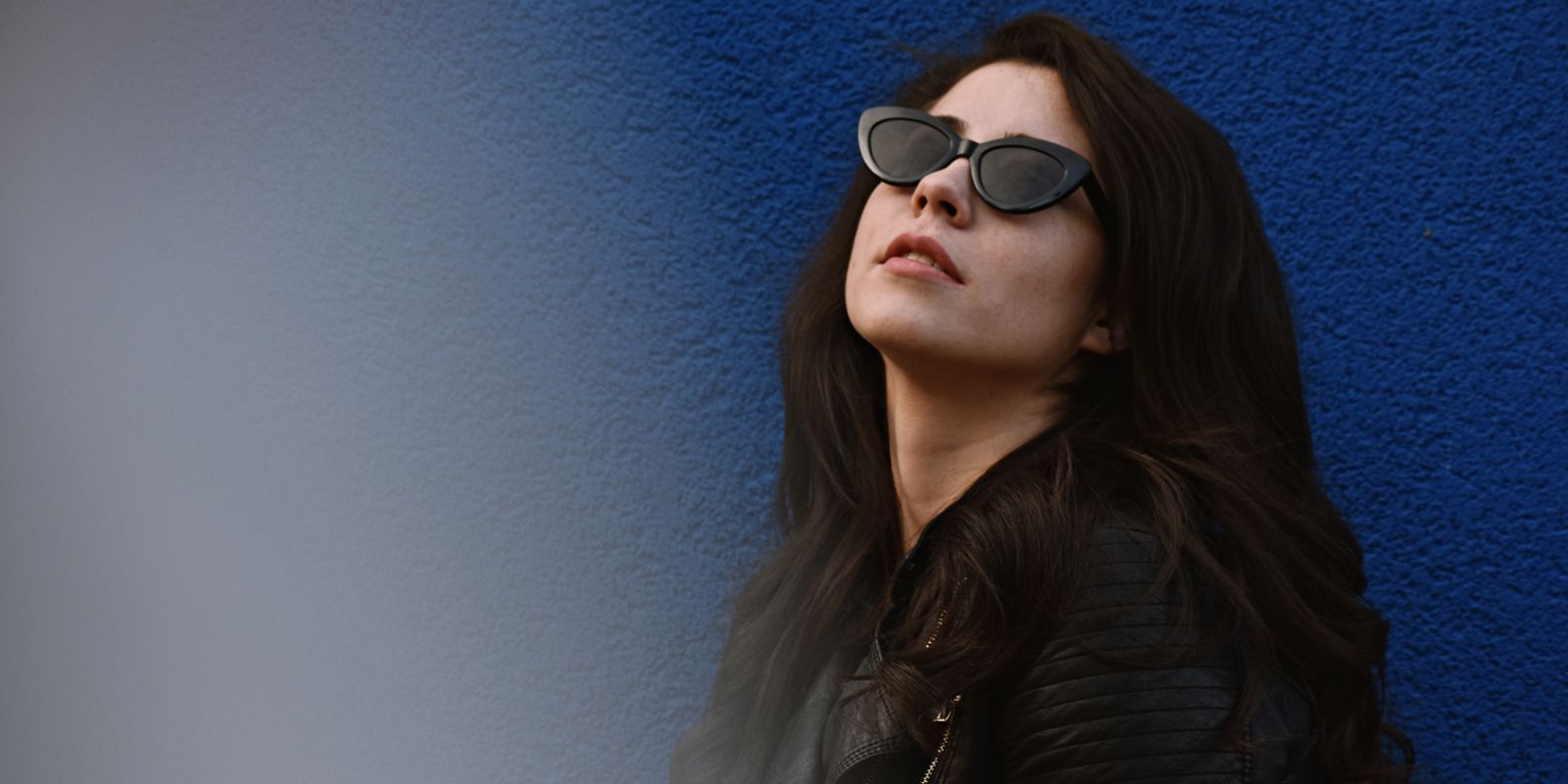 A stylish woman in a leather jacket posing against a vibrant blue wall