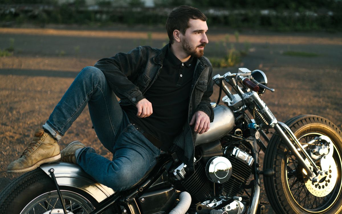 A young man with a beard relaxing beside a custom motorcycle