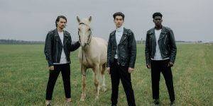 Three men in black leather jackets standing outdoors on open grassland