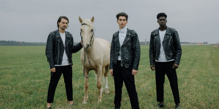 Three men in black leather jackets standing outdoors on open grassland